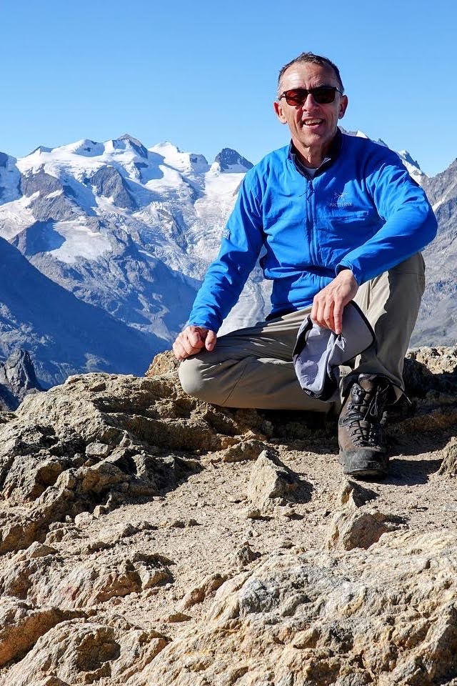 Wanderer sitzt auf Gipfelfelsen vor dem vergletscherten Bernina-Massiv
