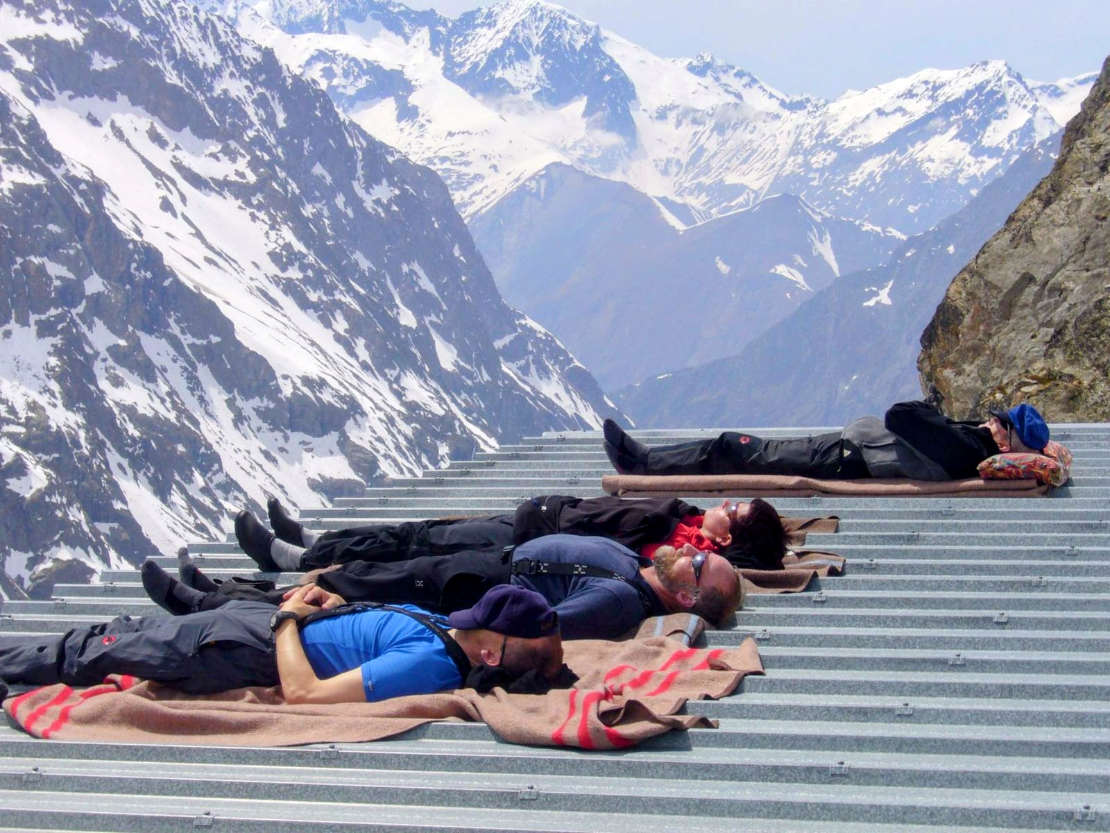 Vier Skitourengänger ruhen sich auf dem Dach der Hütte aus, dahinter das Ecrins-Massiv