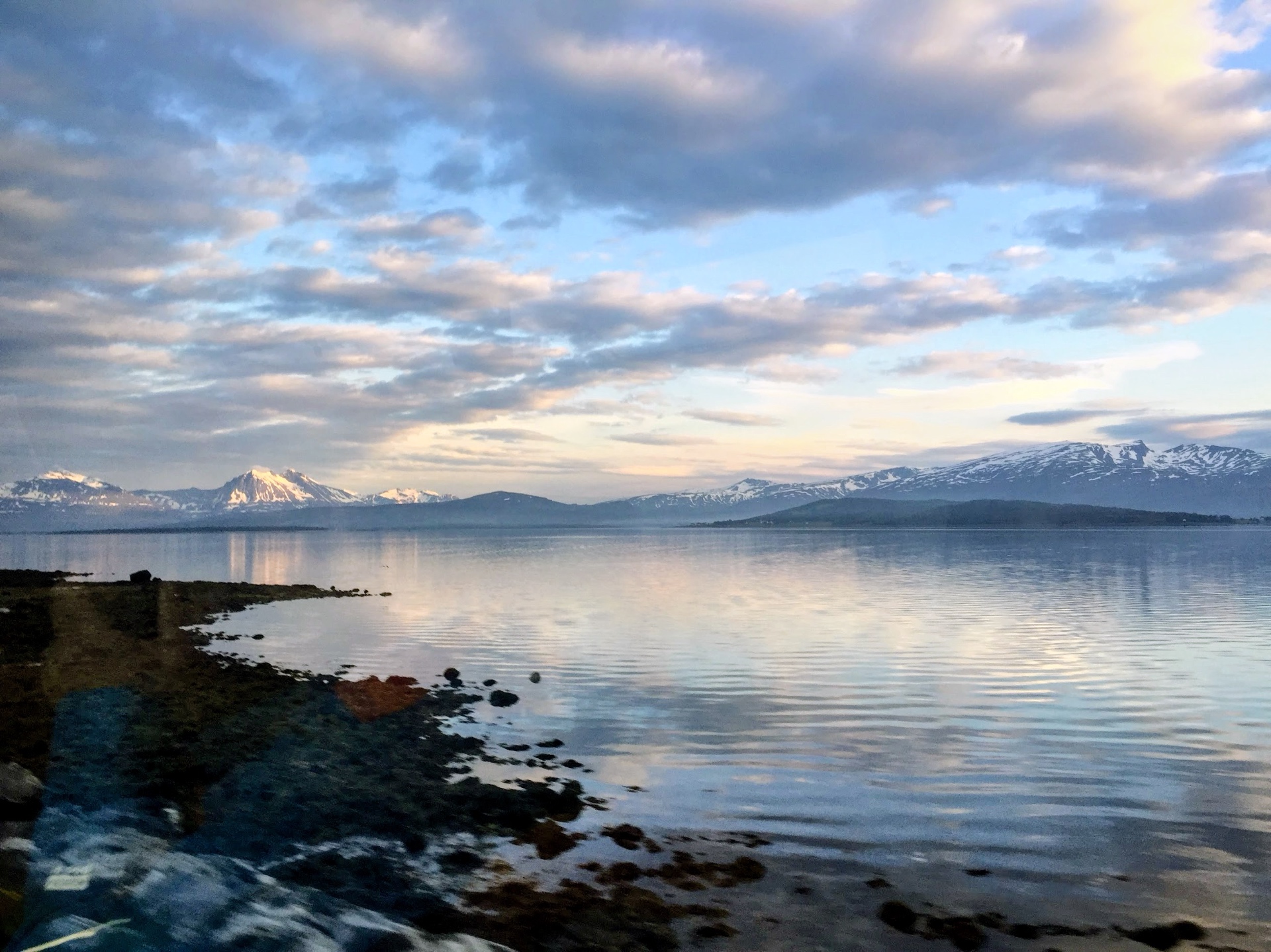 Mitternachtssonne über dem Fjord bei Tromsø mit schneebedeckten Bergen