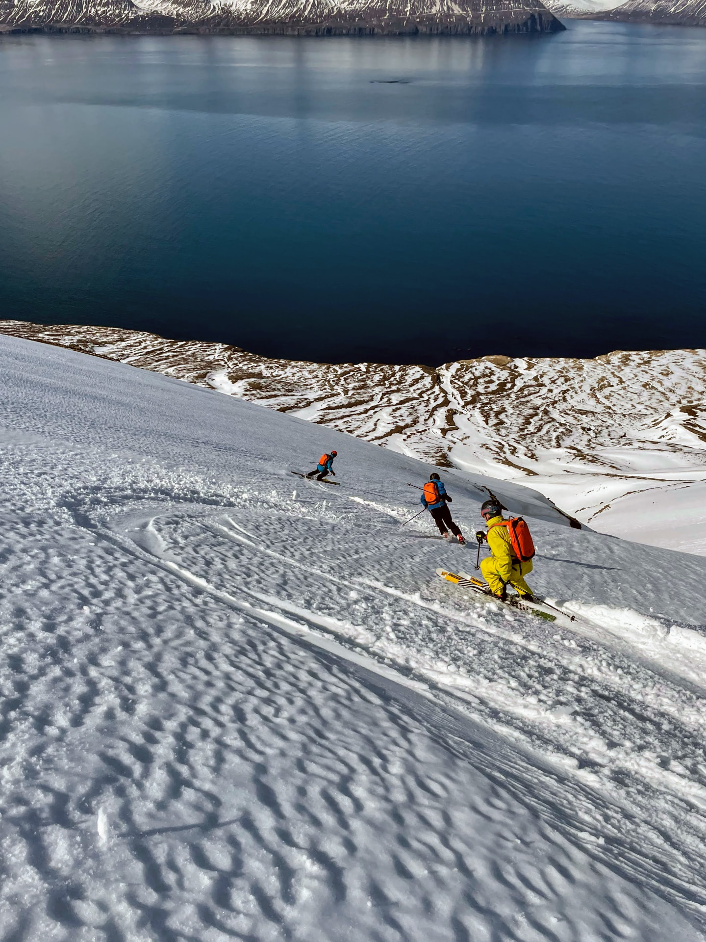 Drei Skifahrer in einem Firnhang direkt über dem Fjord