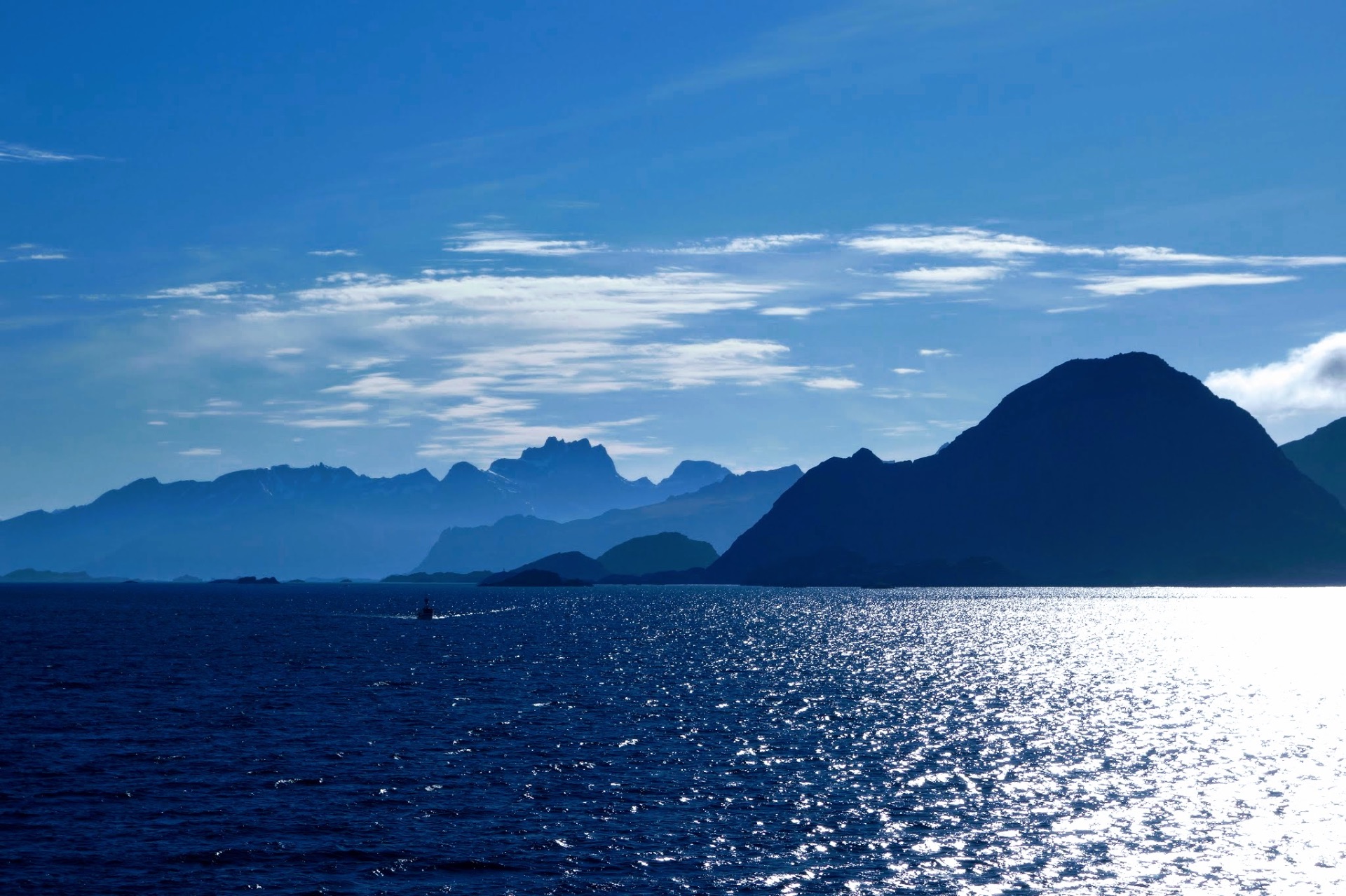 Kleines Boot auf dem glitzernden Fjord vor den blauen Bergsilhouetten Nordnorwegens