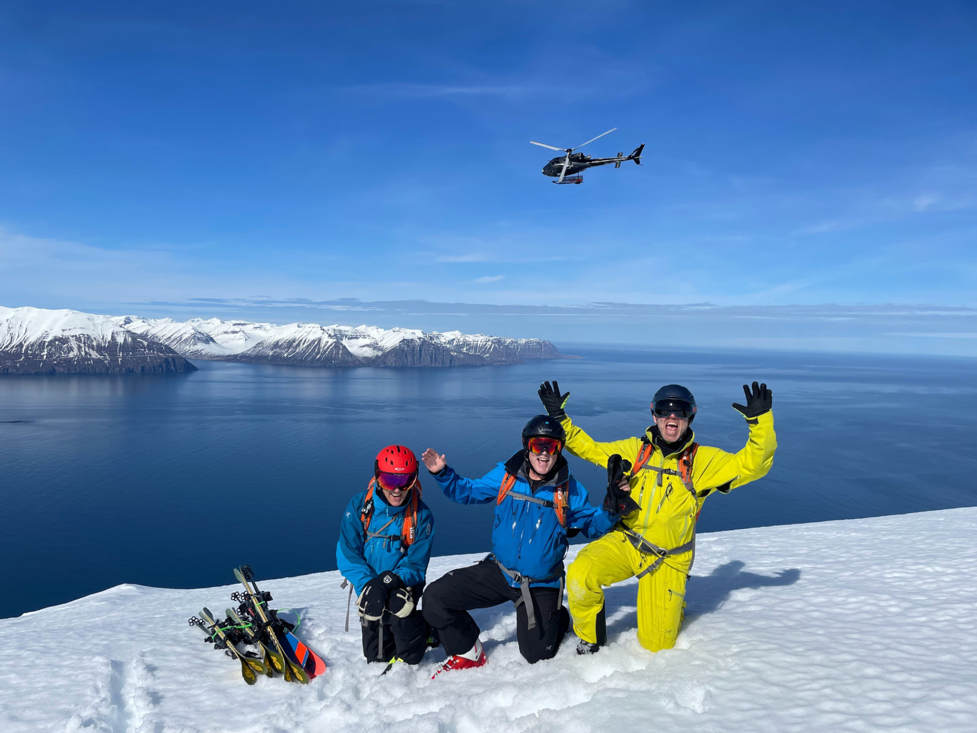 Drei Skifahrer auf einem Gipfel über dem Fjord, Helikopter im Anflug