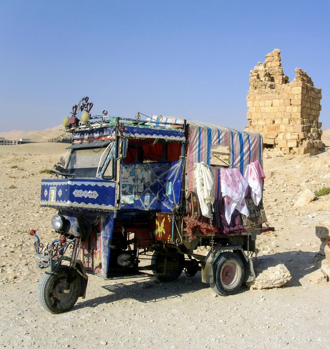 Bunt bemaltes Dreirad-Lastentaxi mit Teppichen vor einer Ruine in Palmyra
