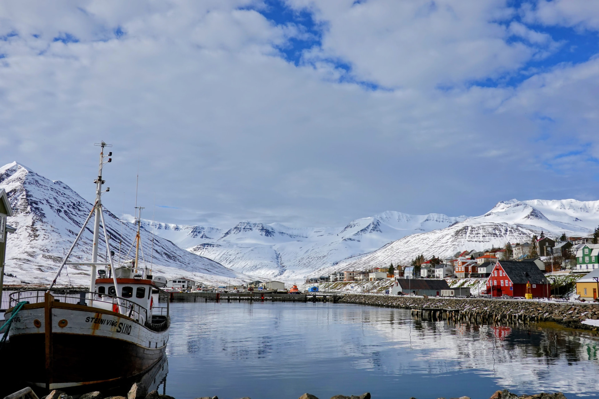 Hafen von Siglufjörður mit Fischerboot und verschneiten Bergen