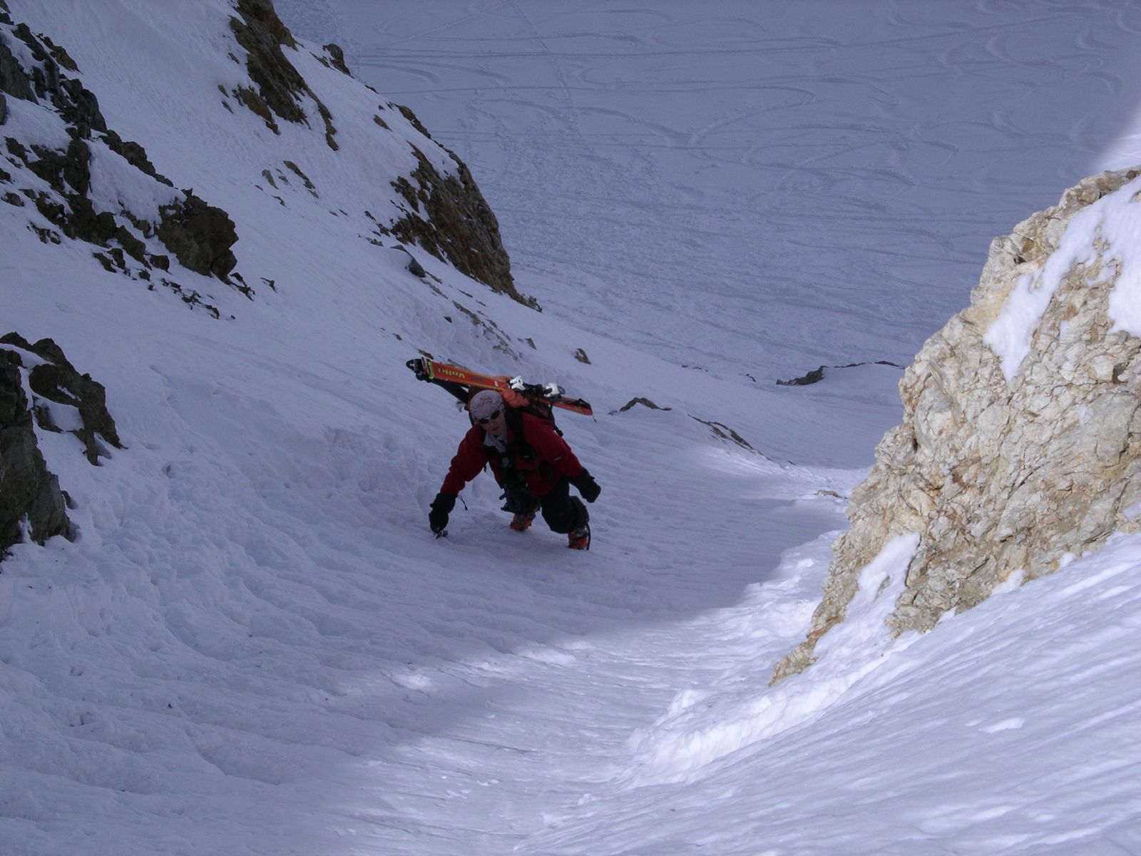 Tourengänger steigt mit Ski am Rucksack ein steiles Couloir hinauf