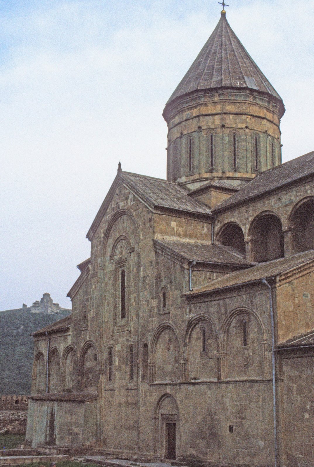 Alte Steinkirche mit Kegeldach in hügeliger Landschaft