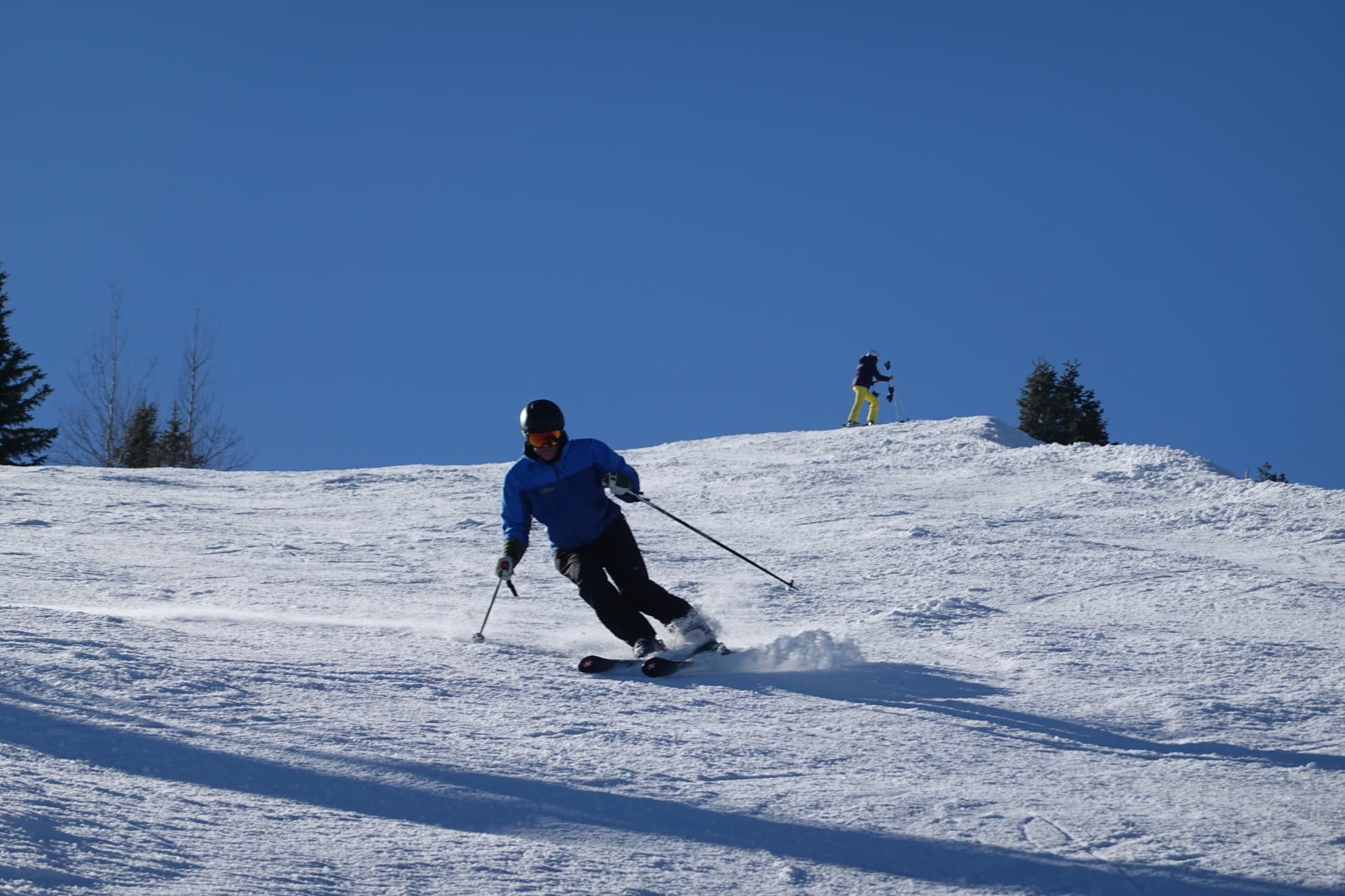 Skifahrer zieht bei blauem Himmel einen Schwung über eine breite Piste
